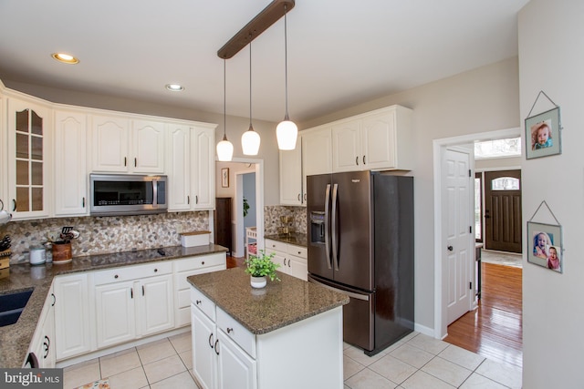 kitchen featuring light tile patterned flooring, stainless steel appliances, white cabinets, glass insert cabinets, and backsplash