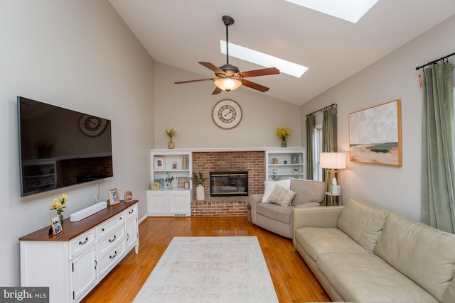 living area with lofted ceiling with skylight, a brick fireplace, a ceiling fan, and light wood-style floors