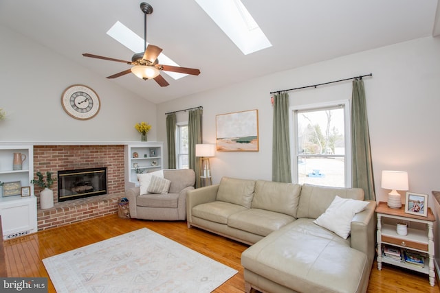 living area featuring lofted ceiling with skylight, ceiling fan, a fireplace, and light wood-style floors