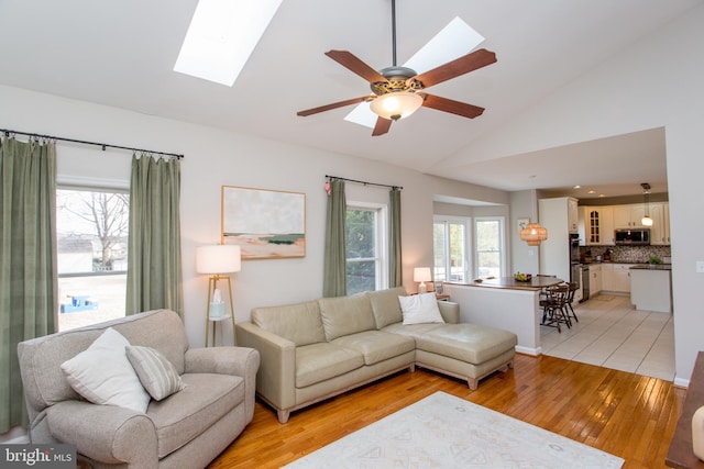 living room with vaulted ceiling with skylight, light wood-type flooring, and ceiling fan