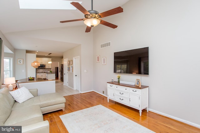 living area featuring light wood finished floors, visible vents, a ceiling fan, and lofted ceiling