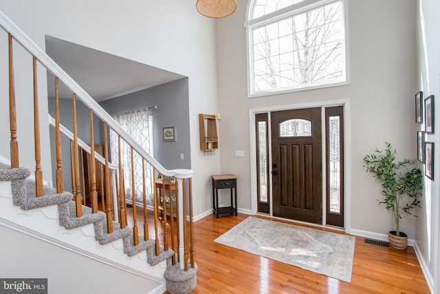 foyer featuring visible vents, wood finished floors, stairway, baseboards, and a towering ceiling