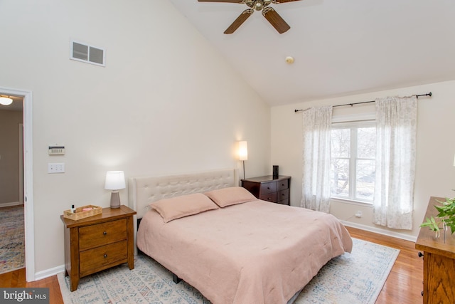 bedroom with baseboards, light wood-style floors, visible vents, and high vaulted ceiling