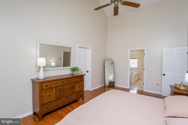 bedroom featuring baseboards, a high ceiling, wood finished floors, and ensuite bathroom