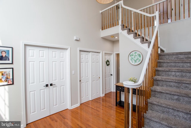 staircase featuring baseboards, a towering ceiling, and wood finished floors