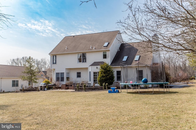 rear view of house with a trampoline, a patio area, and a yard