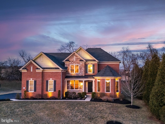 view of front of home with a standing seam roof, a porch, a lawn, brick siding, and metal roof