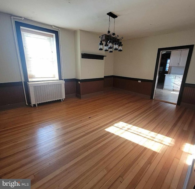 unfurnished dining area featuring a notable chandelier, wainscoting, radiator, and hardwood / wood-style floors