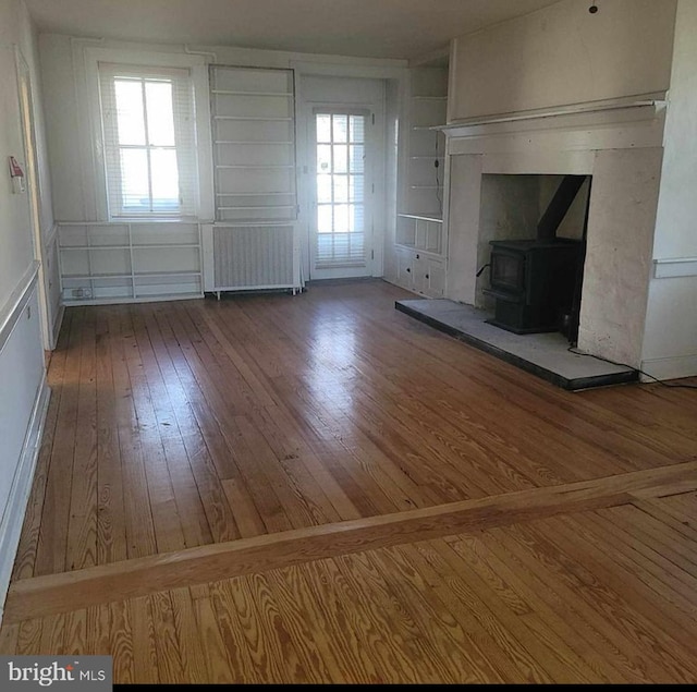 unfurnished living room featuring hardwood / wood-style floors, a wood stove, and radiator