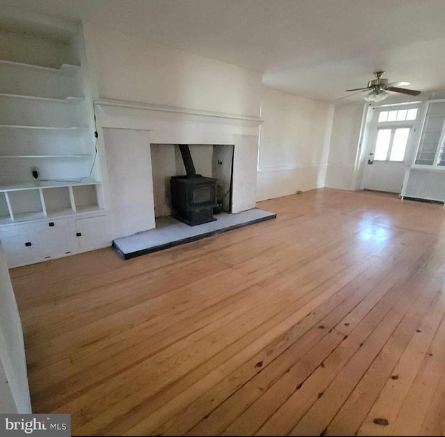 unfurnished living room featuring a wood stove, wood-type flooring, and ceiling fan