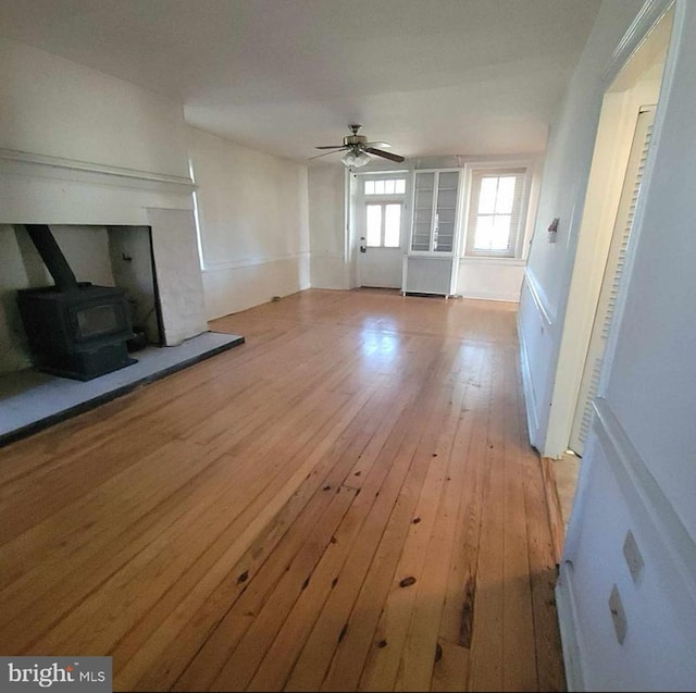 unfurnished living room featuring a ceiling fan, a wood stove, and light wood-style floors