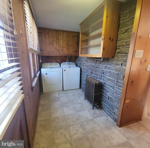 laundry area featuring light floors, radiator heating unit, cabinet space, separate washer and dryer, and wood walls