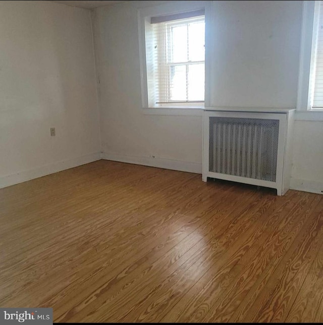 unfurnished room with a healthy amount of sunlight, radiator heating unit, baseboards, and wood finished floors