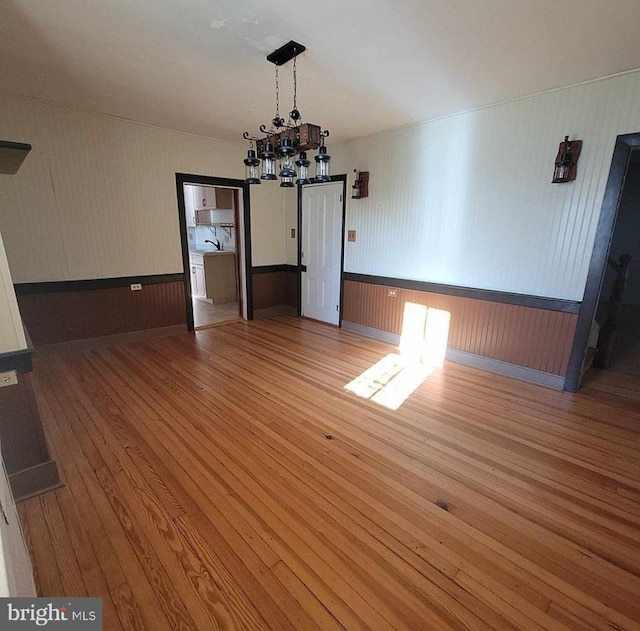 unfurnished dining area featuring a wainscoted wall, a notable chandelier, and hardwood / wood-style floors