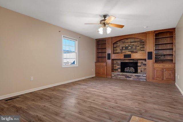 unfurnished living room with visible vents, built in shelves, wood finished floors, a fireplace, and baseboards