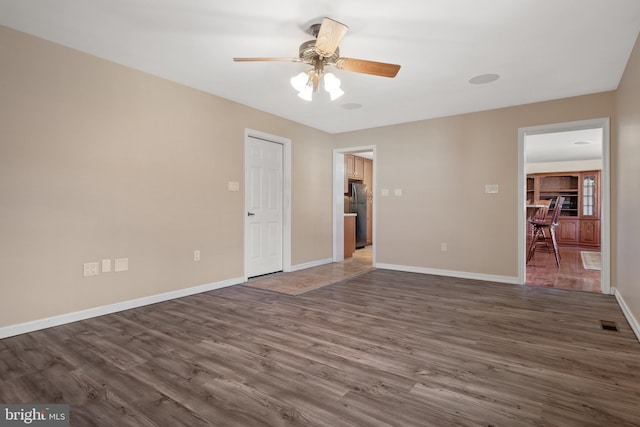 unfurnished room with a ceiling fan, visible vents, baseboards, and dark wood-style flooring