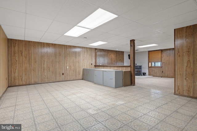 kitchen with a paneled ceiling, wooden walls, light floors, and a wood stove