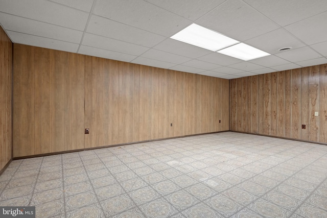 unfurnished room with a drop ceiling, baseboards, light floors, and wood walls