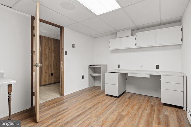 unfurnished office with light wood-type flooring, a paneled ceiling, baseboards, and built in desk