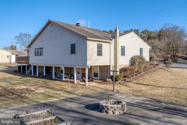 rear view of house featuring a lawn, a chimney, and an outdoor fire pit