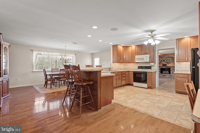 kitchen featuring white microwave, light wood finished floors, a breakfast bar, a peninsula, and electric stove