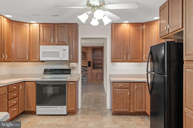 kitchen featuring electric stove, white microwave, brown cabinets, and freestanding refrigerator