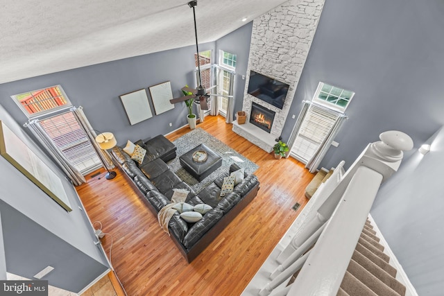 living area with a ceiling fan, wood finished floors, baseboards, high vaulted ceiling, and a stone fireplace