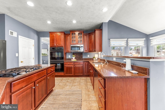 kitchen with visible vents, a peninsula, a sink, glass insert cabinets, and appliances with stainless steel finishes