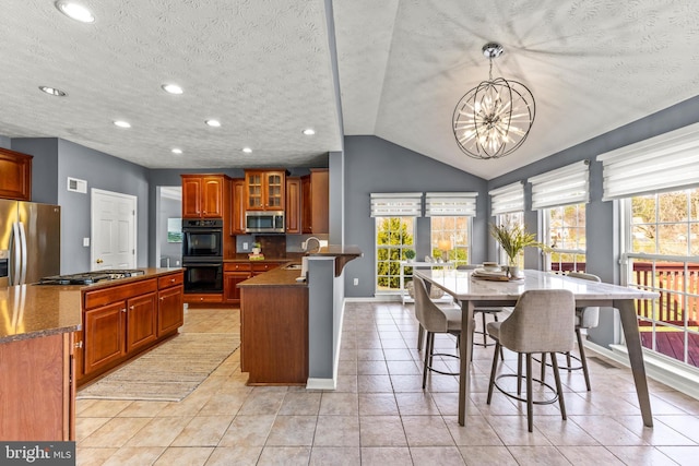 kitchen featuring brown cabinets, appliances with stainless steel finishes, a peninsula, a notable chandelier, and a sink