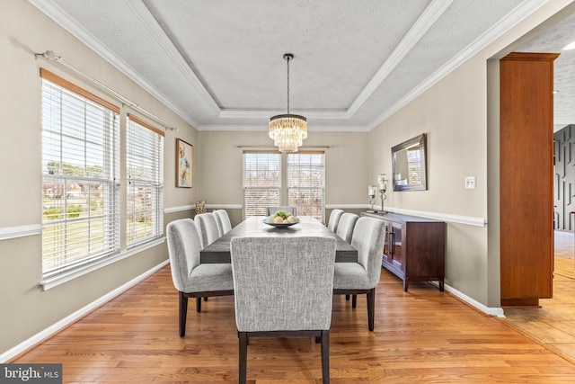 dining space with crown molding, baseboards, light wood-style flooring, a notable chandelier, and a raised ceiling