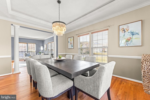dining room with crown molding, baseboards, light wood-type flooring, a notable chandelier, and ornate columns