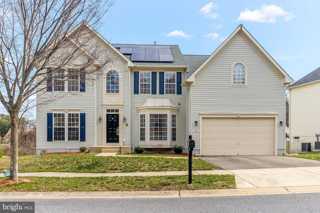 view of front facade featuring cooling unit, roof with shingles, solar panels, an attached garage, and concrete driveway