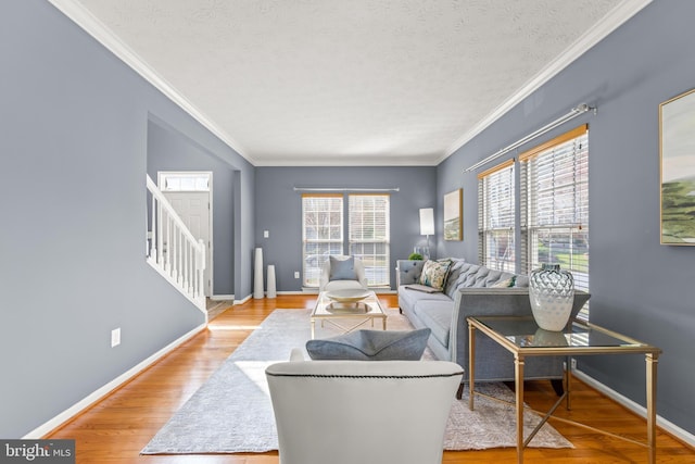 living room featuring a textured ceiling, wood finished floors, stairway, crown molding, and baseboards
