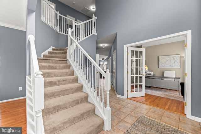 stairway featuring tile patterned flooring, french doors, baseboards, and a towering ceiling