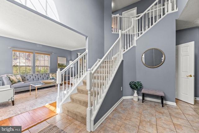 stairs featuring tile patterned floors, crown molding, baseboards, and a towering ceiling