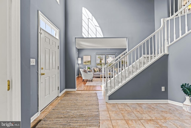 tiled foyer with baseboards, a high ceiling, and stairs