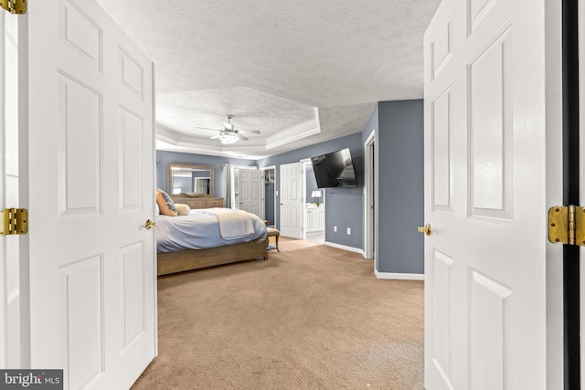 bedroom featuring a textured ceiling, a raised ceiling, baseboards, and light carpet