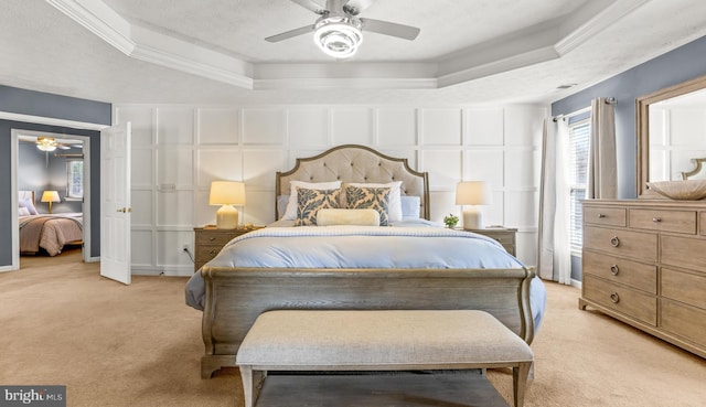 bedroom with a ceiling fan, crown molding, a decorative wall, a raised ceiling, and light colored carpet