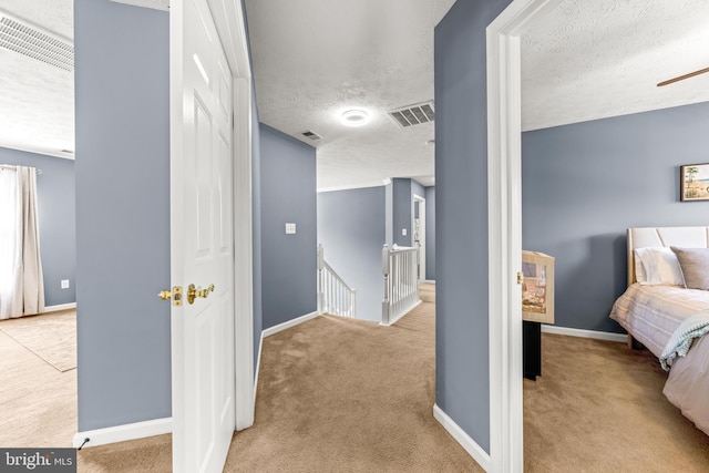 corridor with visible vents, baseboards, carpet, an upstairs landing, and a textured ceiling