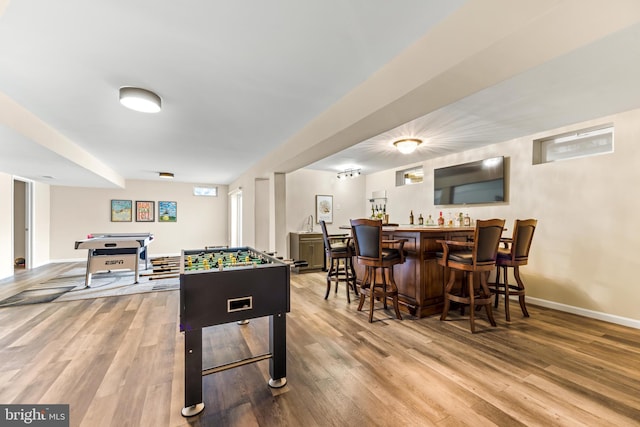 game room featuring baseboards, indoor bar, and wood finished floors