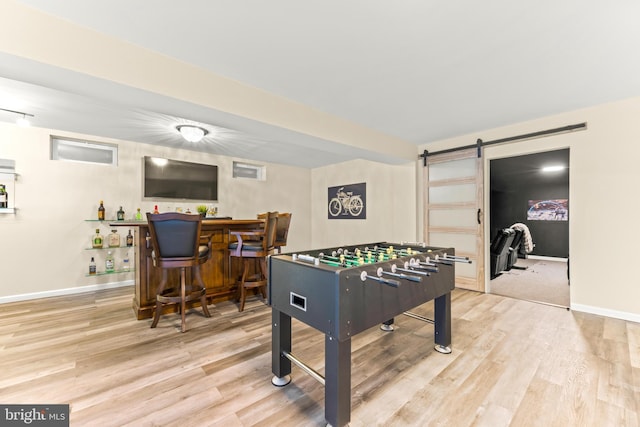 game room with a dry bar, baseboards, light wood-style floors, and a barn door