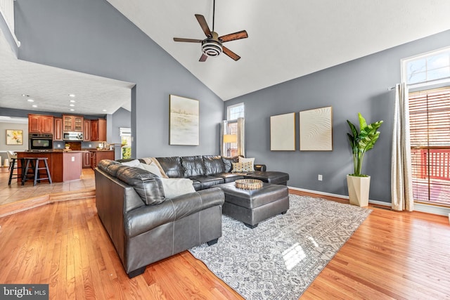 living area with a wealth of natural light, light wood finished floors, high vaulted ceiling, and ceiling fan