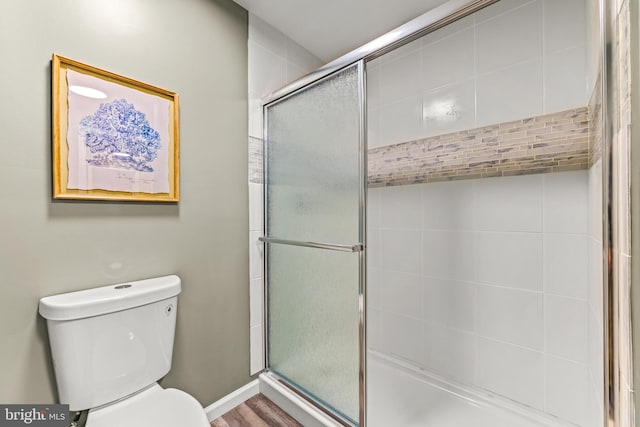 full bathroom with toilet, wood finished floors, baseboards, and a tile shower