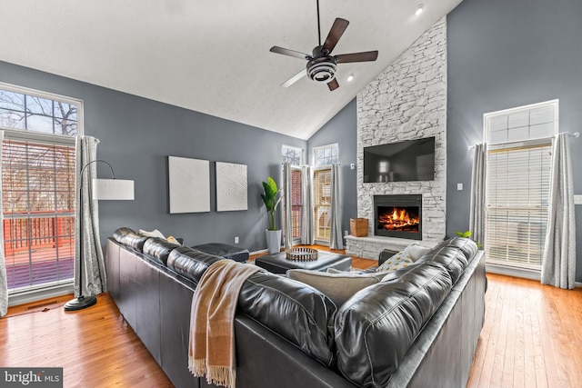 living room with high vaulted ceiling, a fireplace, a ceiling fan, and light wood finished floors