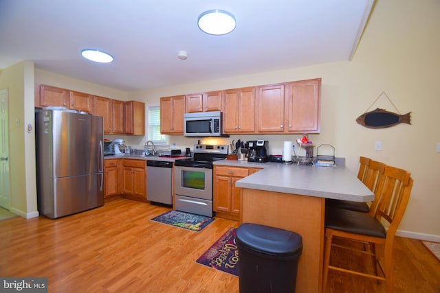 kitchen with a peninsula, a sink, light wood-style floors, appliances with stainless steel finishes, and a kitchen breakfast bar