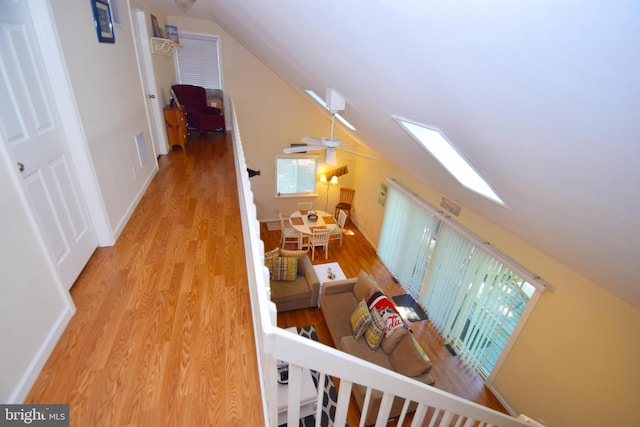 hall featuring visible vents, vaulted ceiling with skylight, baseboards, and wood finished floors