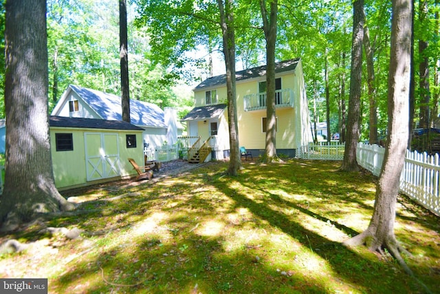 rear view of property featuring an outbuilding, a storage shed, a balcony, and fence