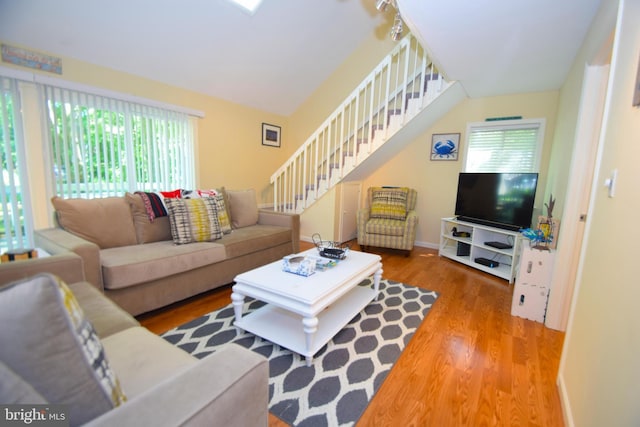 living area with a wealth of natural light, stairway, baseboards, and wood finished floors