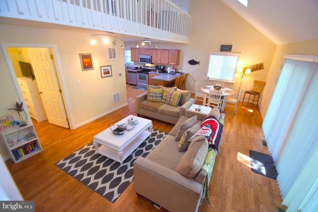 living room featuring light wood-type flooring, visible vents, baseboards, and high vaulted ceiling