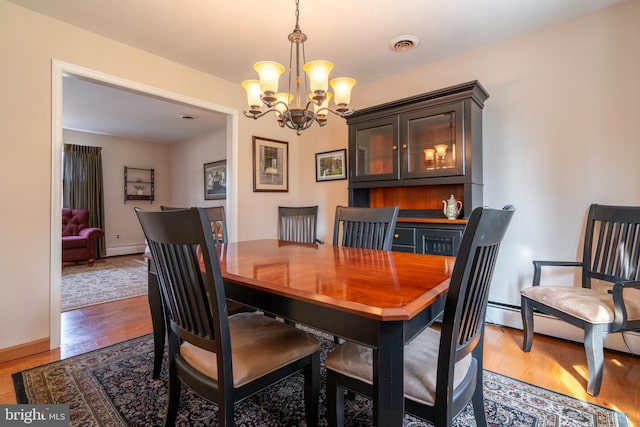 dining area with a chandelier, baseboards, visible vents, and wood finished floors